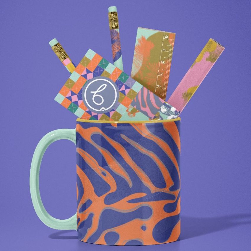 Mug mockup with bold orange and blue zebra pattern, filled with colorful stationery items like pencils, a ruler, and cards, on a purple background.