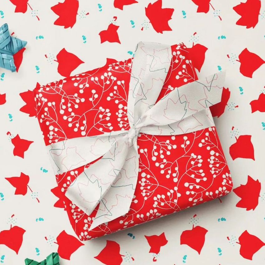 Square gift box mockup wrapped in red paper with white berry and leaf pattern, topped with a white ribbon, on a festive background.