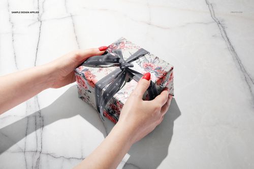PSD mockup of a wrapped gift box featuring a floral design and black ribbon, displayed on a marble tabletop.