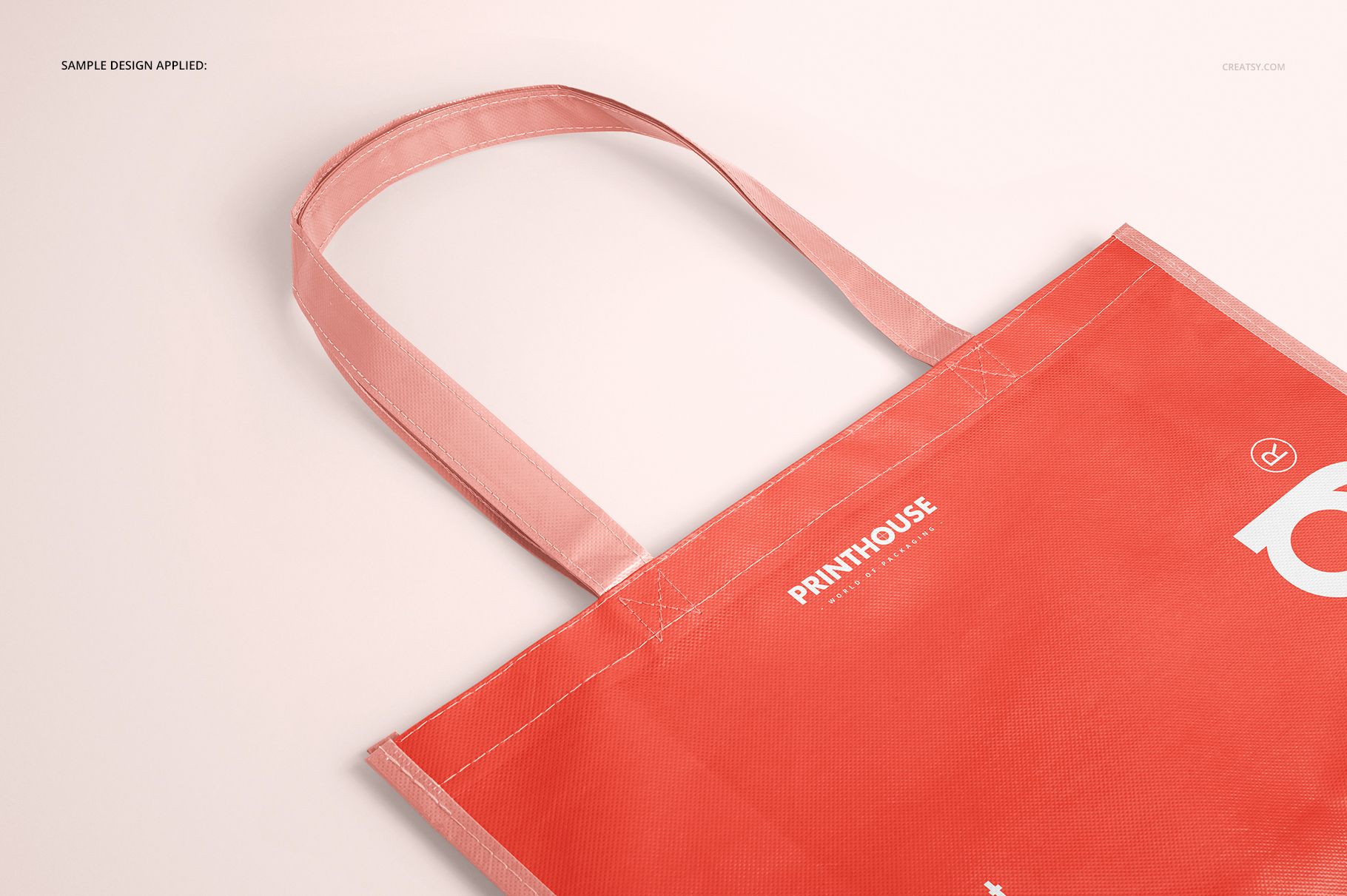 Front angled view of a laminated non-woven tote bag mockup in coral pink with visible stitching and handles.
