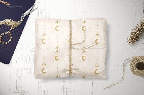 Gift wrapping tissue paper mockup featuring a gold geometric and eye pattern, tied with twine, shown from above.