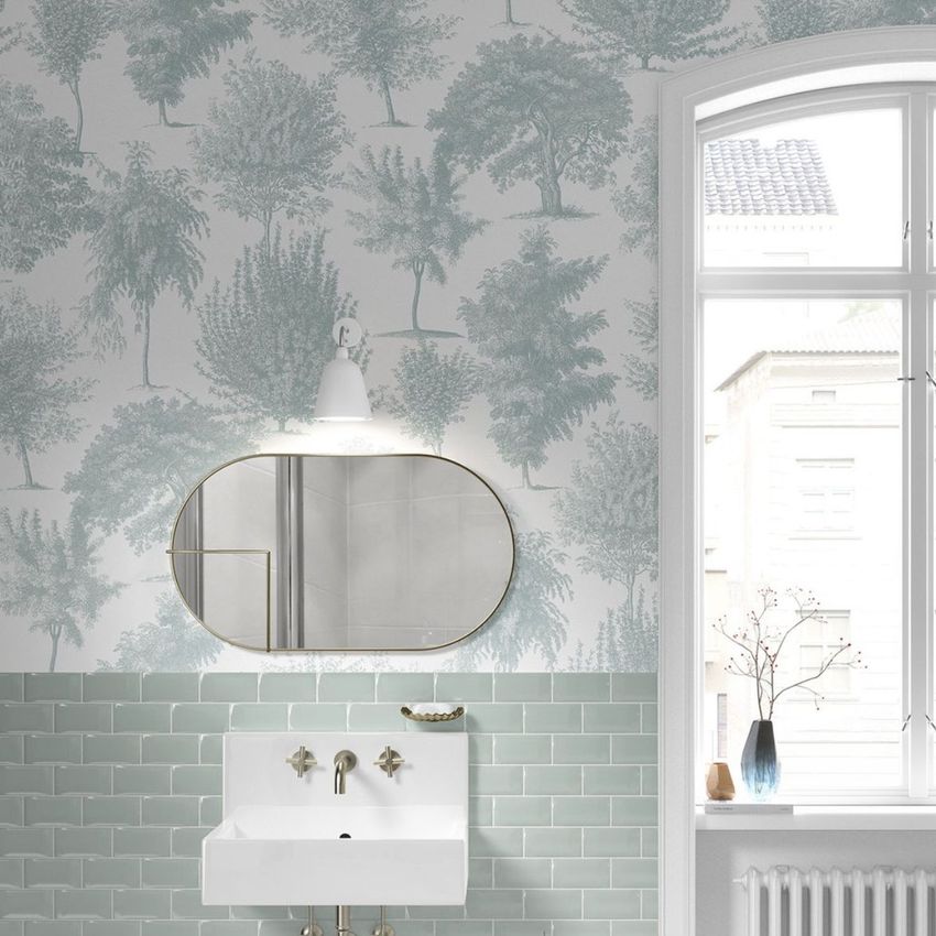 Vintage bathroom mockup featuring a white sink, oval mirror, and green subway tile with tree-patterned wallpaper above.