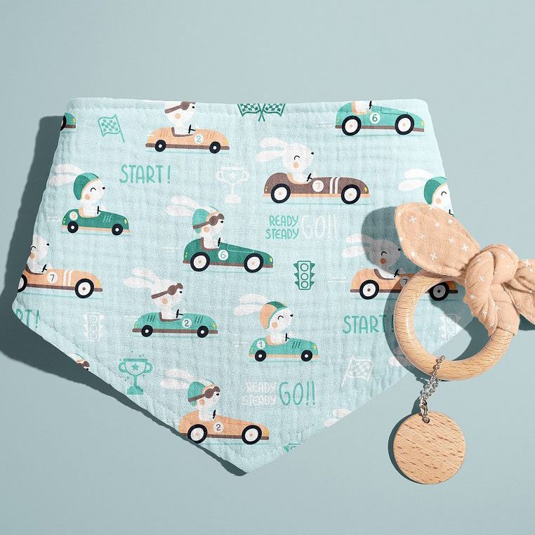 Baby muslin bandana mockup featuring a pastel blue fabric with a playful bunny race car pattern, shown with a wooden teether on a light blue background.