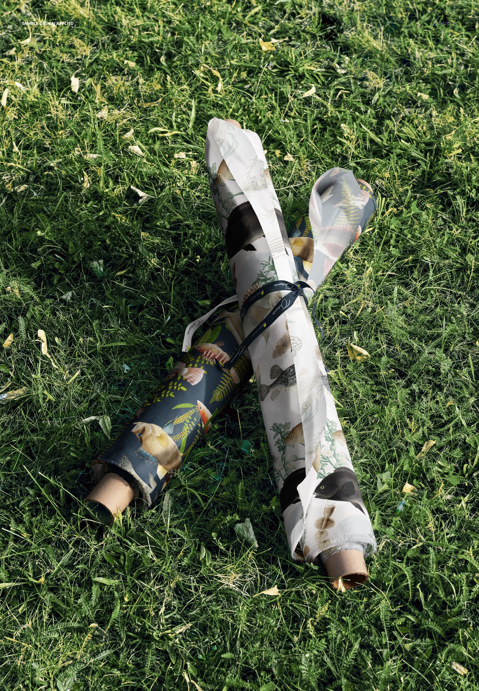 Two patterned fabric rolls crossed and tied together, displayed on a textured grass surface, PSD mockup.