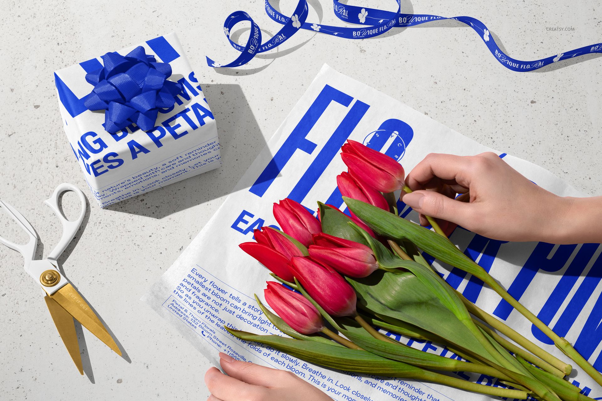 PSD mockup showing red tulips on white tissue wrapping paper with bold blue lettering, next to gift wrapping supplies.