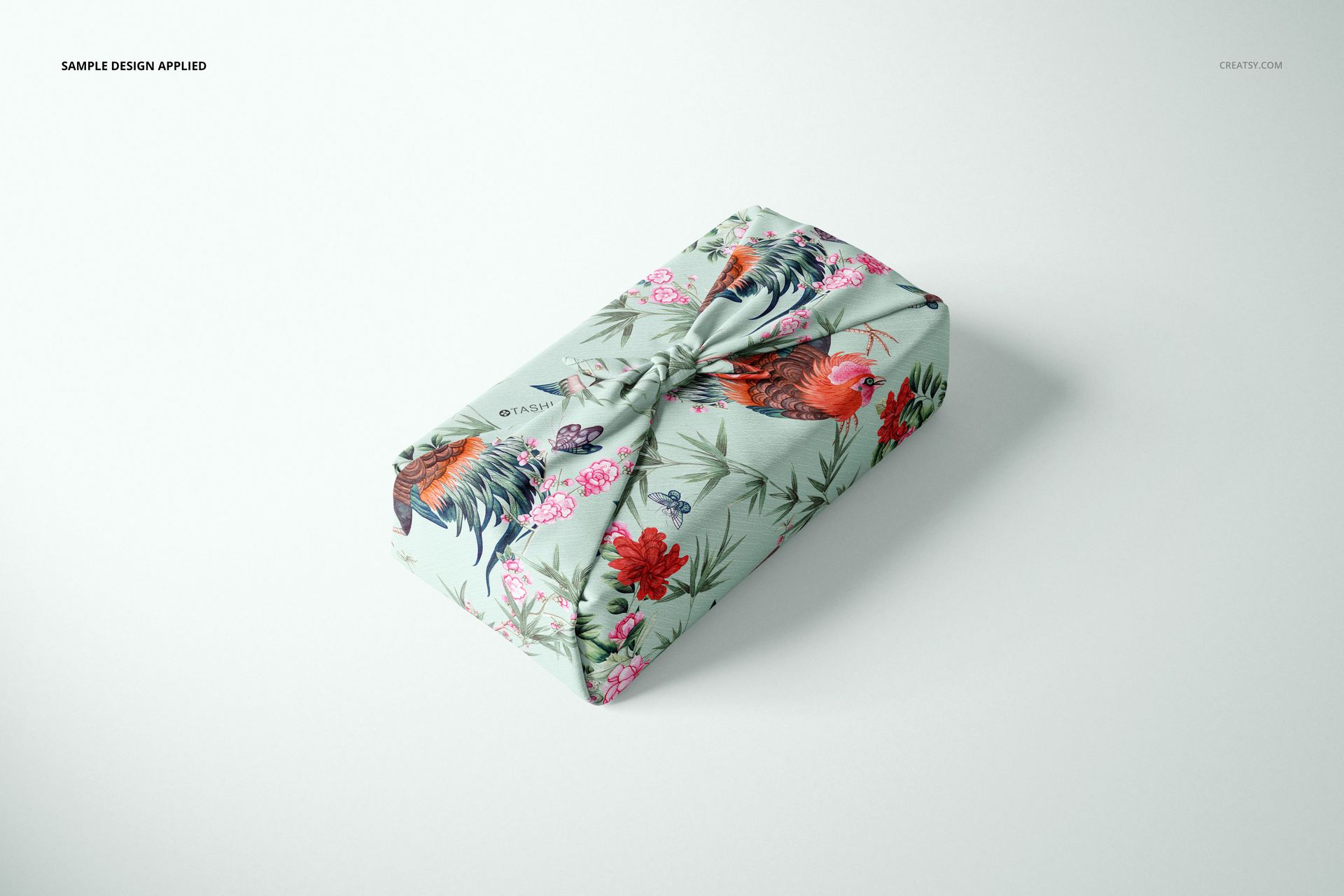 Furoshiki fabric wrap mockup featuring a colorful rooster and flower design, shown from a slightly elevated angle.