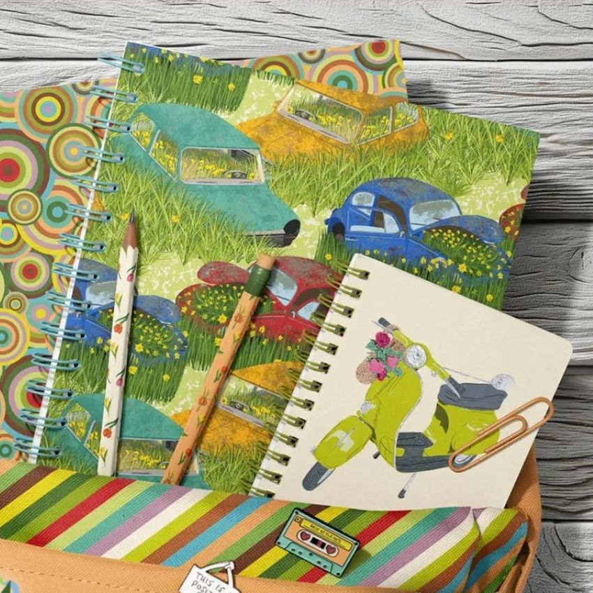 School backpack mockup with spiral notebooks featuring colorful illustrated covers, two pencils, and a wooden background.
