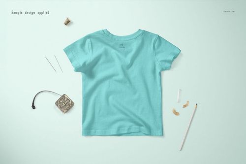 Light blue baby T-shirt mockup shown from the back, placed on a soft blue background with sewing accessories nearby.