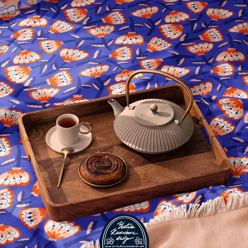Microfiber comforter mockup featuring a bold blue and orange floral pattern, with a wooden tray holding a teapot, cup of tea, and pastry on top.