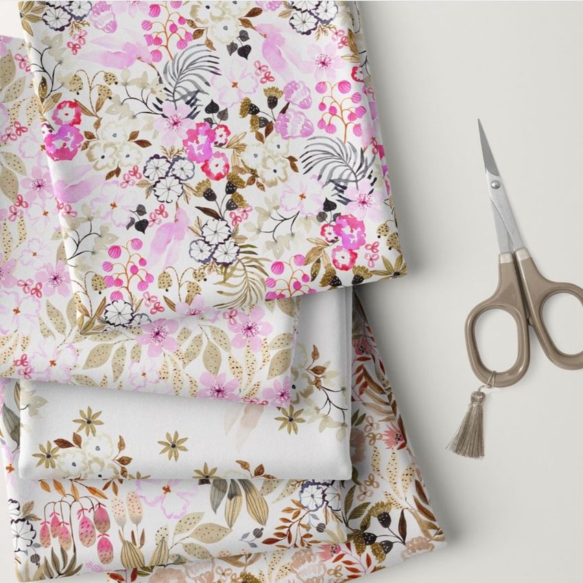 Folded fabrics mockup featuring three pieces of cloth with watercolor floral patterns in pink, white, and beige tones on a light surface.
