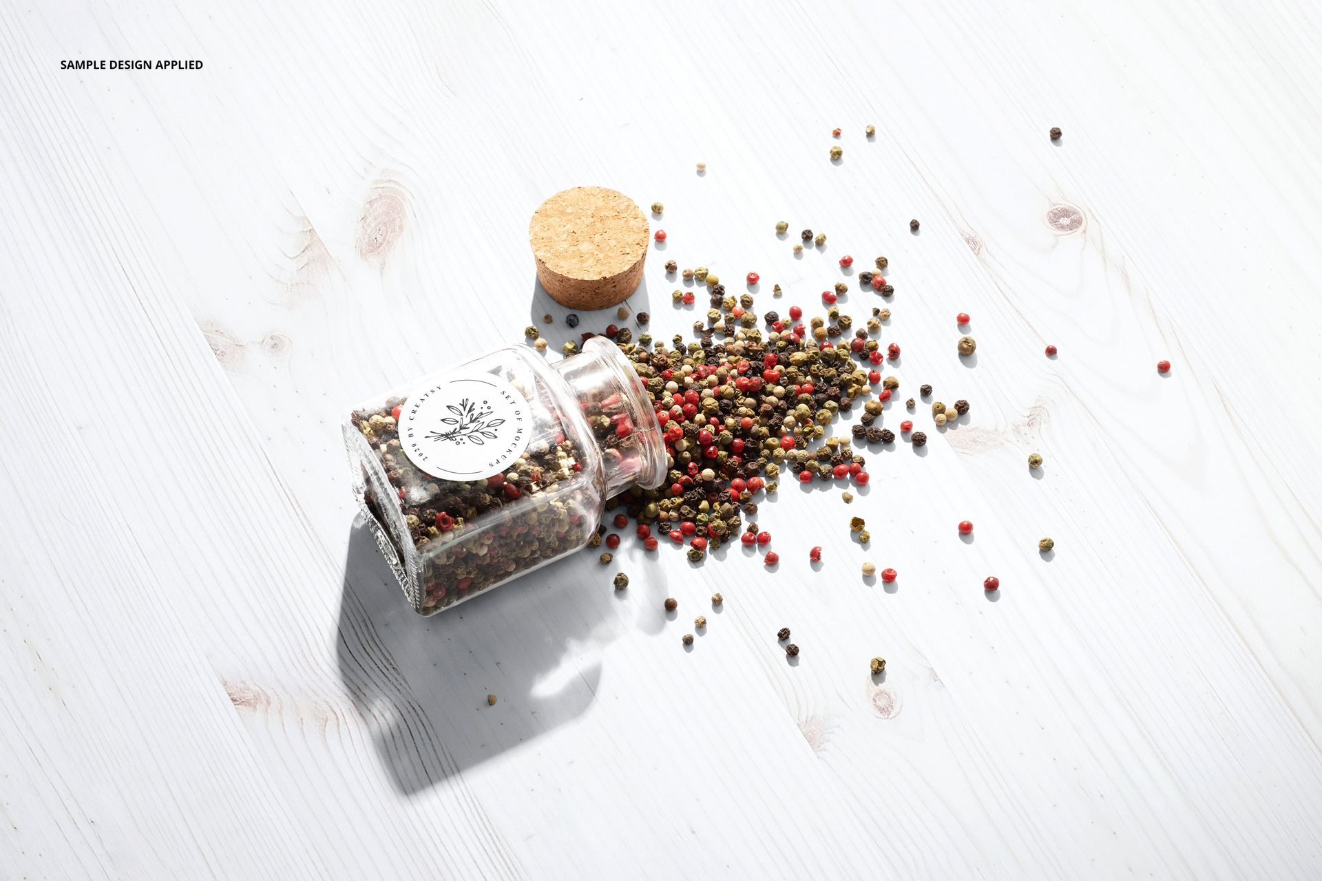 Round spice jar label mockup featuring a glass jar on its side with colorful peppercorns spilled on a white wood surface.