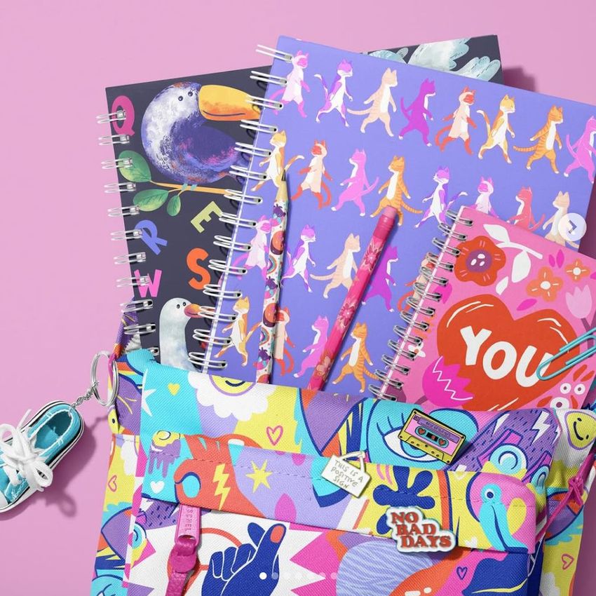 Colorful school backpack mockup with spiral notebooks featuring vibrant animal and abstract designs on a pink background.