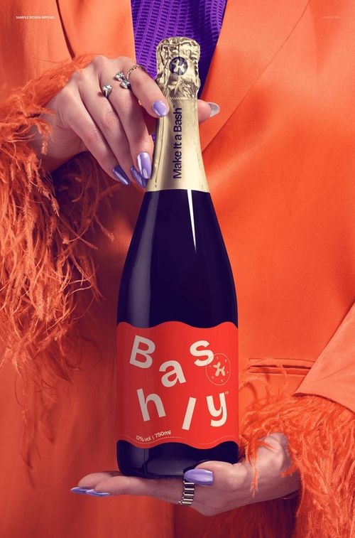 Front view of a champagne bottle mockup gripped by hands wearing an orange feathered jacket and purple top.