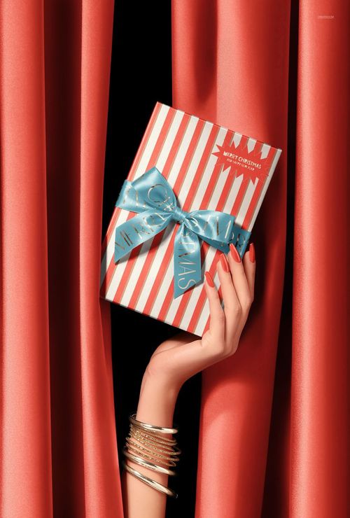 Christmas PSD mockup featuring a wrapped gift with blue ribbon, presented by a hand emerging from red drapes.