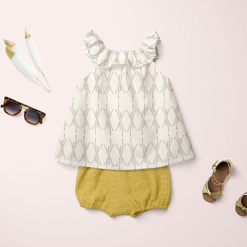 Baby summer set mockup featuring a patterned sleeveless top and yellow shorts arranged on a pale pink background with sunglasses, sandals, and decorative feathers.