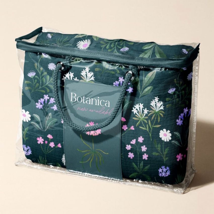 Newborn swaddle wrap mockup featuring a floral-patterned fabric inside a clear plastic zippered bag with a green handle.