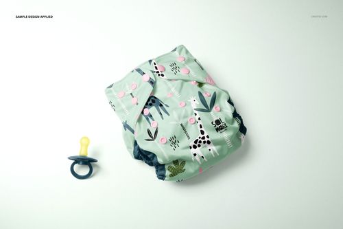 PSD mockup of a reusable baby diaper in soft green with pink buttons and whimsical prints, displayed with a pacifier.