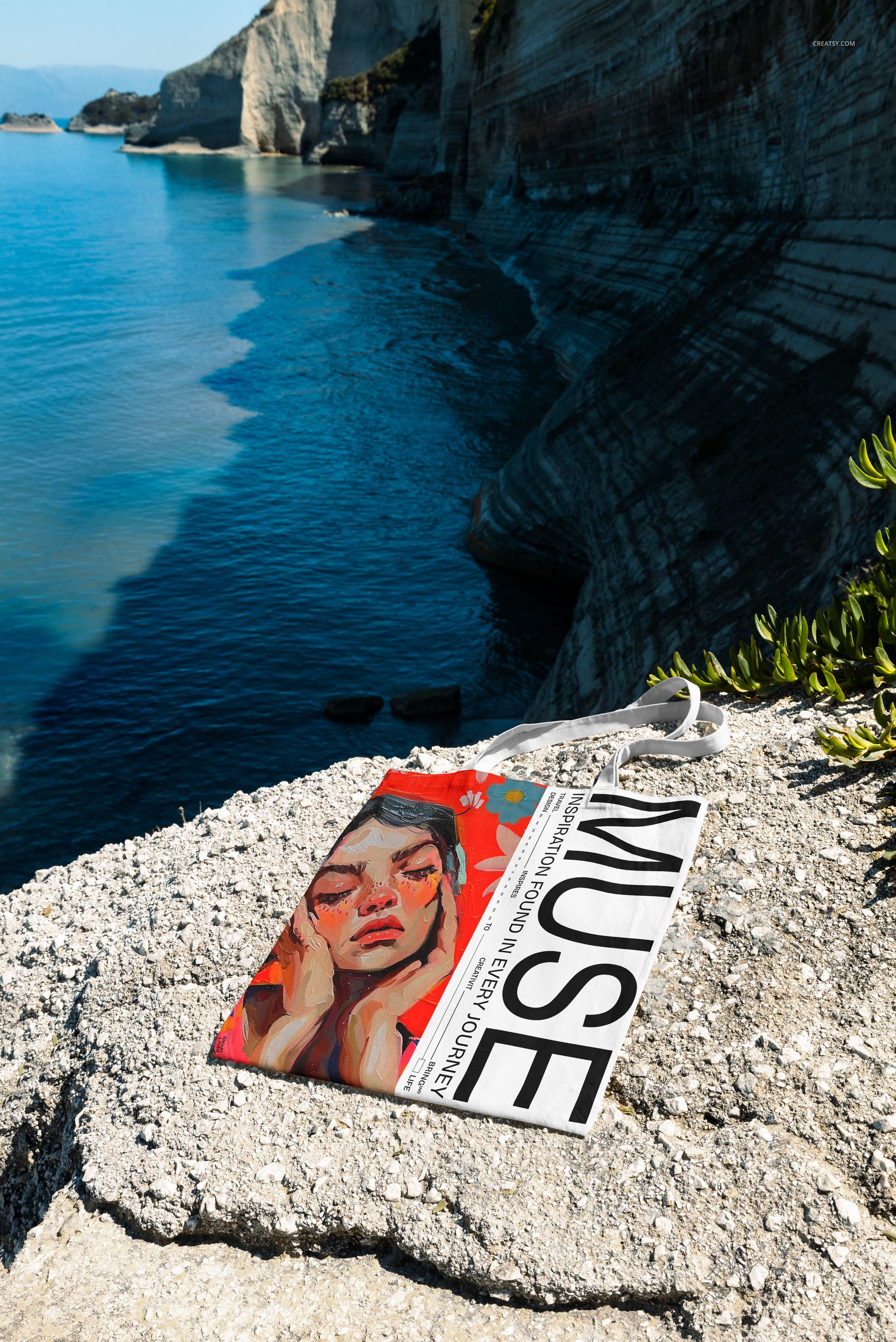 Outdoor scene featuring a tote bag mockup placed on a sunlit stone ledge overlooking dramatic seaside cliffs.