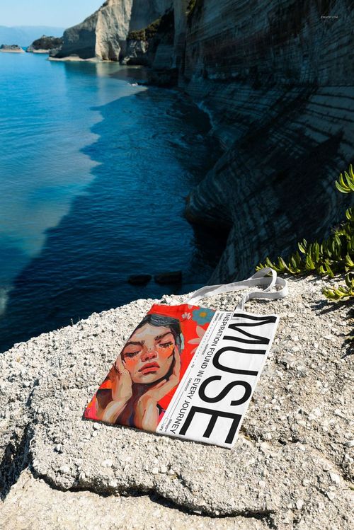 Outdoor scene featuring a tote bag mockup placed on a sunlit stone ledge overlooking dramatic seaside cliffs.