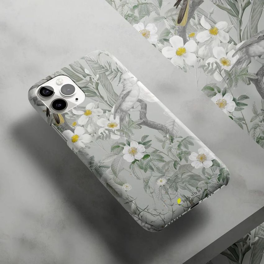 Glossy iPhone 11 Pro snap case mockup with a botanical and bird illustration, placed on a marble surface with matching wallpaper.
