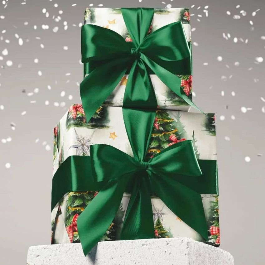 Two Christmas gifts wrapped in festive paper with green ribbons are stacked on a white pedestal, with falling snow in the background.