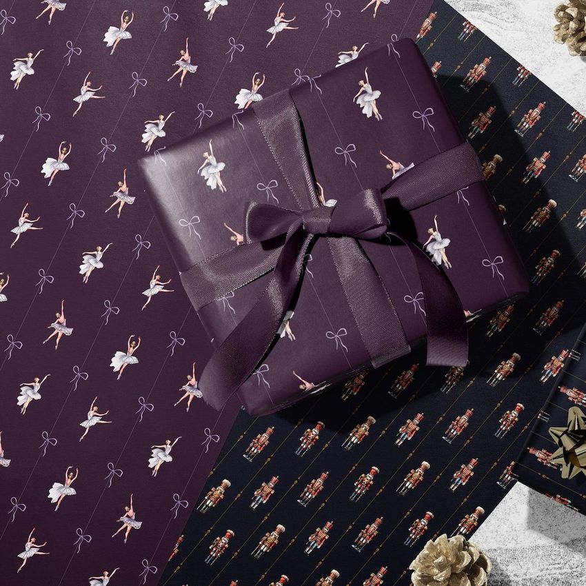 Wrapping paper mockup featuring a gift box wrapped in dark purple paper with ballerina patterns, set on matching sheets.
