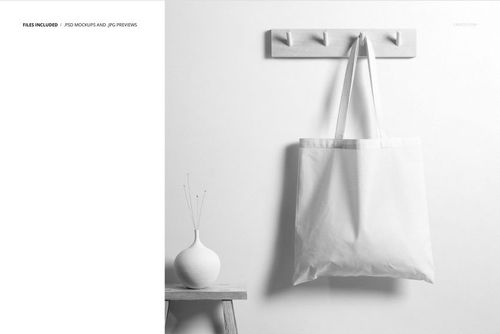 Tote bag mockup displayed against a light wall, featuring a wooden rack, a simple vase, and a stool, photographed from the front.