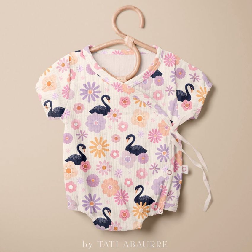 Muslin onesie mockup hanging on a wooden hanger, featuring a swan and floral pattern in pastel colors on a beige background.