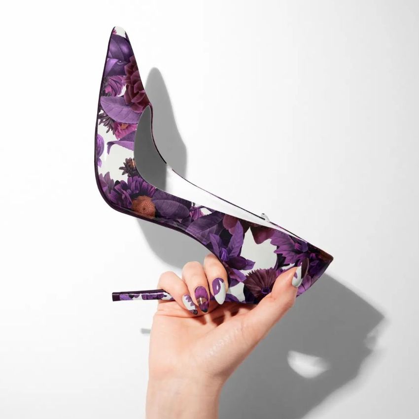 High heel shoe mockup with a purple floral pattern held in a hand, shown against a plain white background.