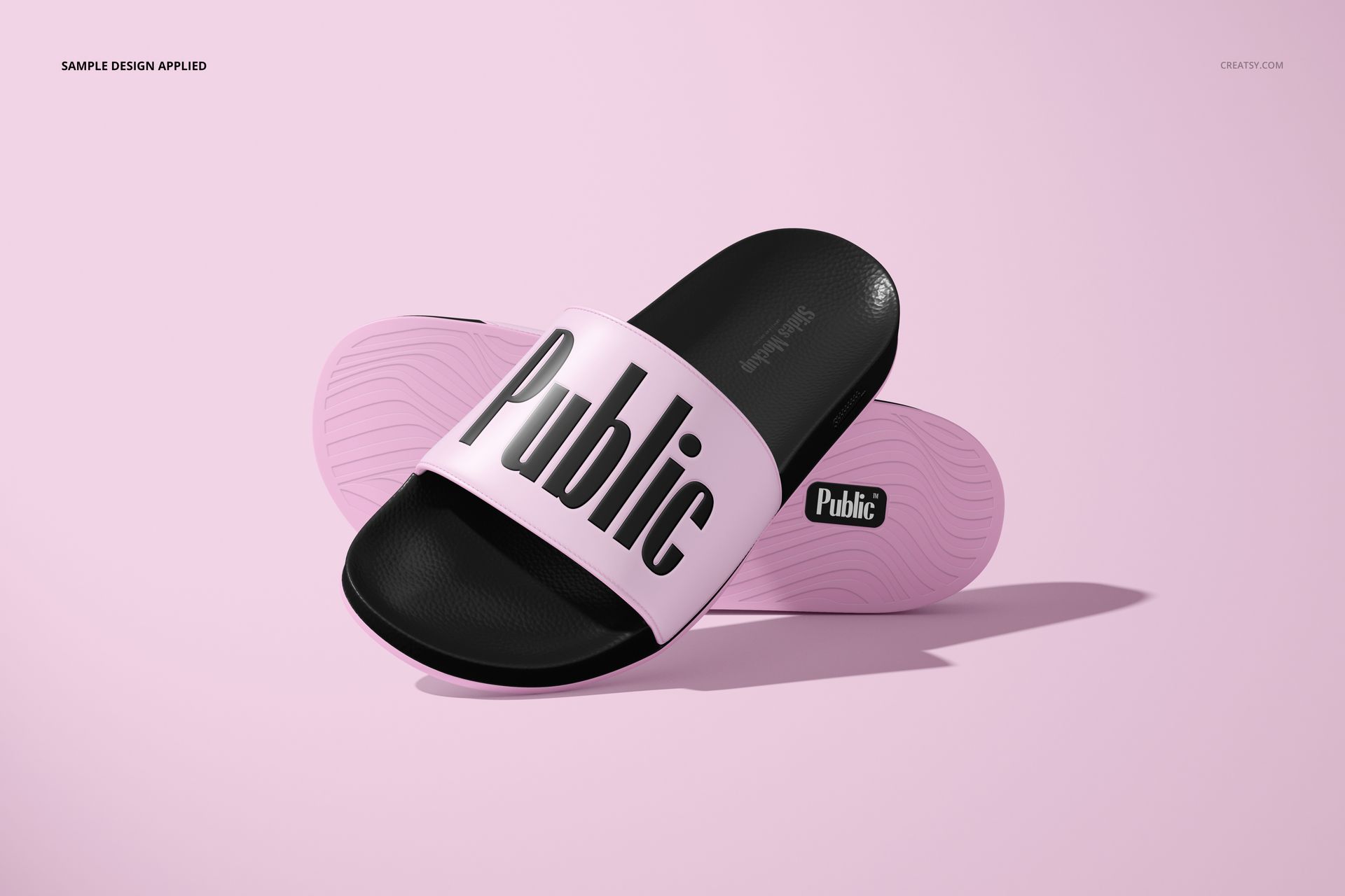 Slip-on slide sandals mockup featuring black soles and light pink straps with bold black text, shown on a pink surface.