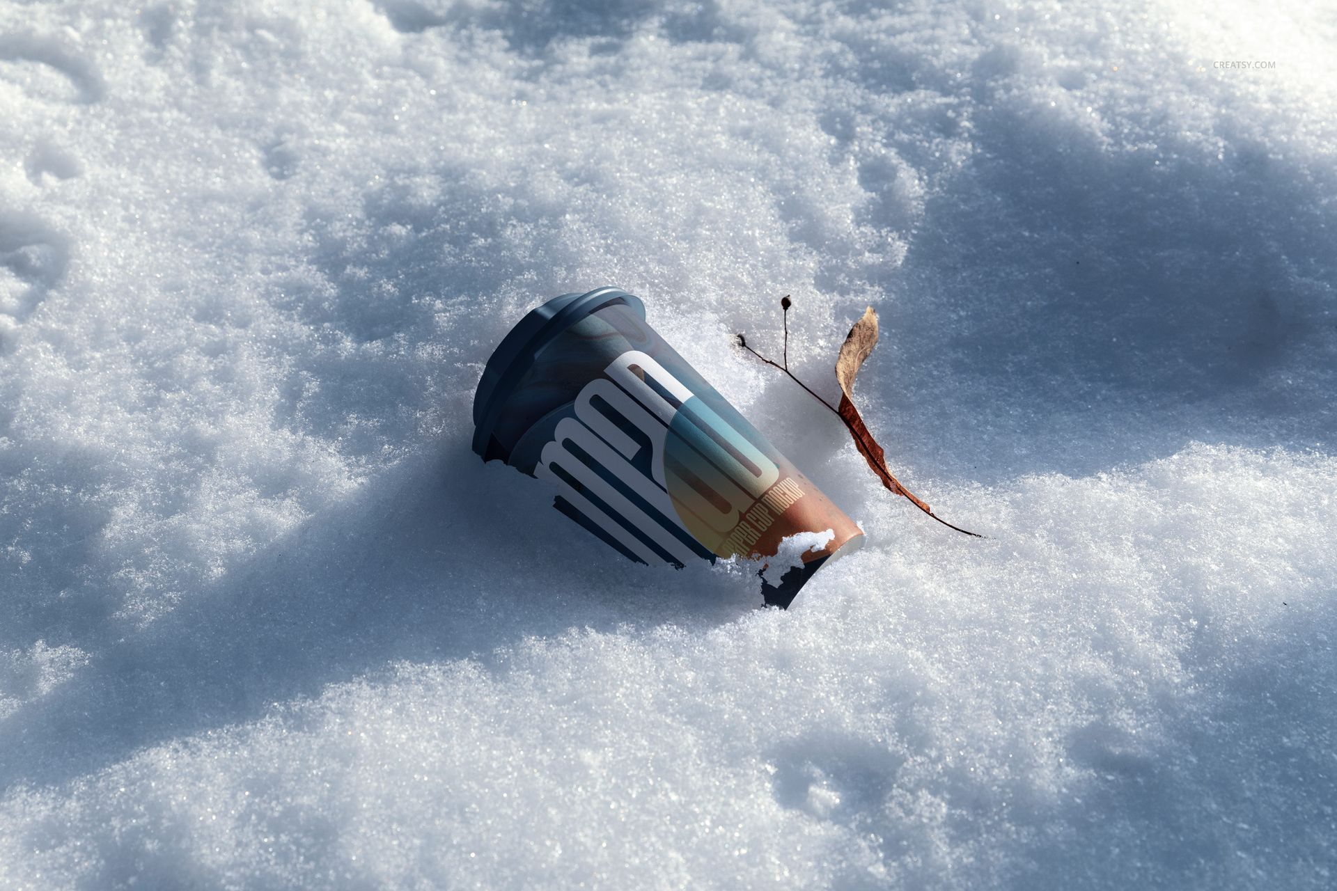 Winter-themed PSD mockup featuring a paper cup with a dark lid resting in fresh snow beside a dried leaf.