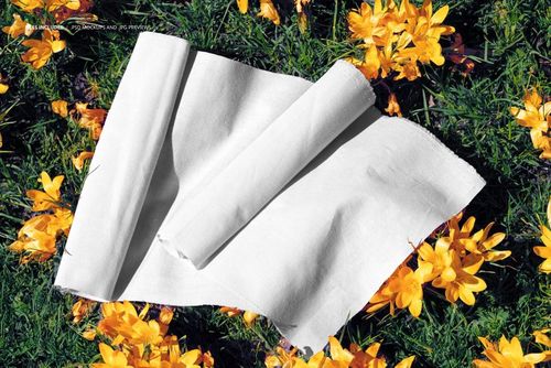 Rolled white fabric displayed on green grass with scattered yellow flowers, viewed from above in a mockup scene.