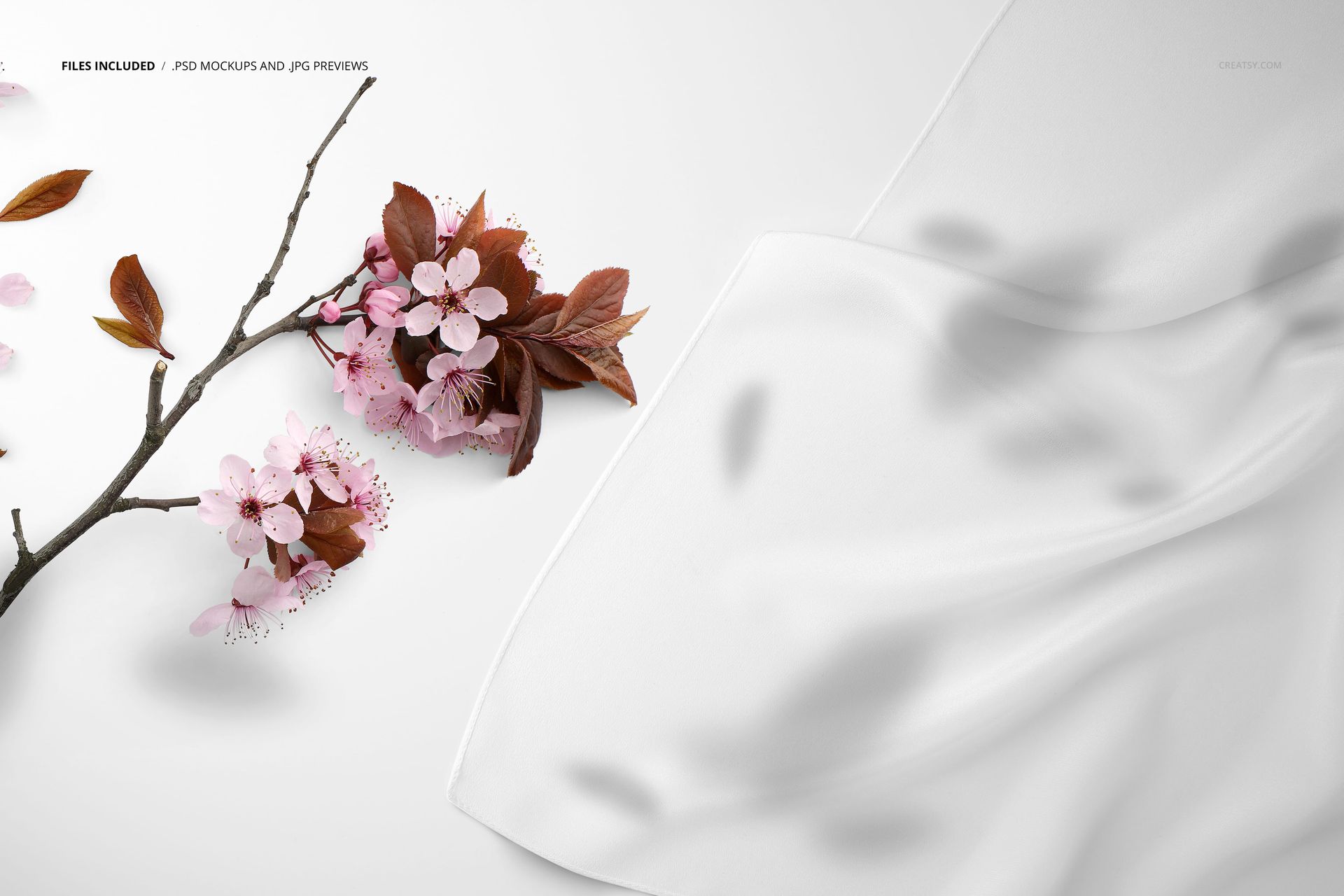 Close-up view of a white silk scarf mockup beside a branch with pink flowers and brown leaves on a light surface.