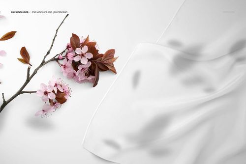 Close-up view of a white silk scarf mockup beside a branch with pink flowers and brown leaves on a light surface.