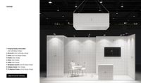 Trade show booth mockup with white tiled walls, reception counter, chairs, table, and overhead hanging display.