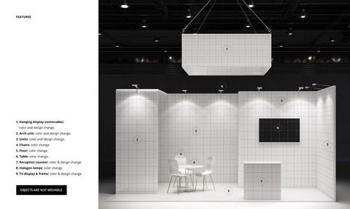 Trade show booth mockup with white tiled walls, reception counter, chairs, table, and overhead hanging display.