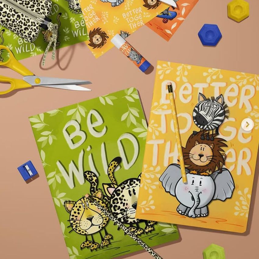 Stationery mockup featuring two A4 notebooks with safari animal illustrations, surrounded by scissors, glue stick, pencil, and erasers on a beige surface.