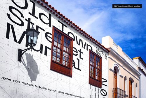 Large street mural mockup on a white building wall with wooden windows and a black lamp, viewed from below.
