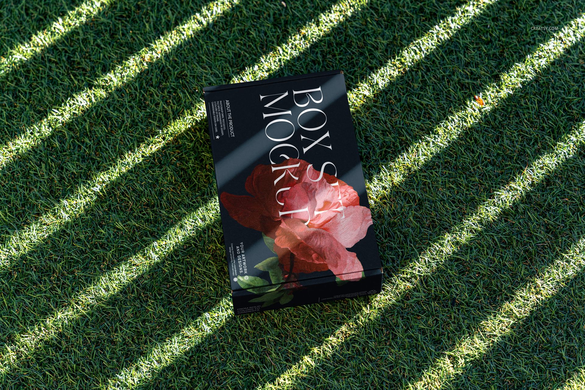 Black mailing box mockup with large red flower graphic placed outdoors on textured grass with sunlight stripes.