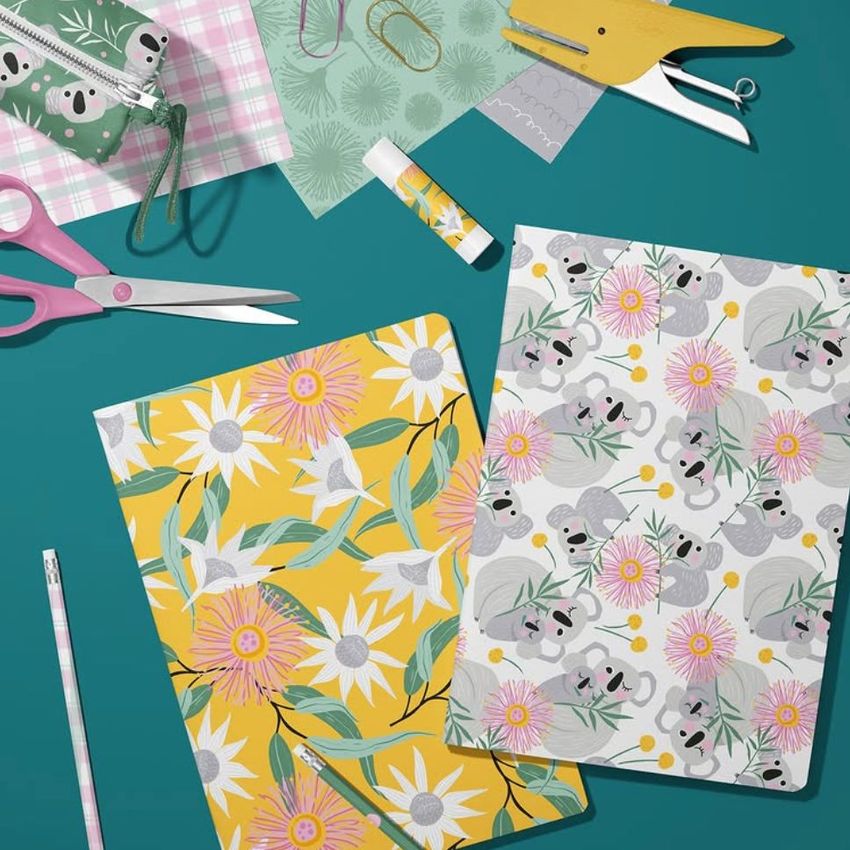 Stationery mockup featuring two A4 notebooks with floral and koala patterns, surrounded by scissors, paper, and office supplies on a teal surface.