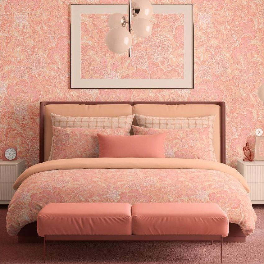 Bedroom scene bedding mockup featuring a bed with peach and pink patterned duvet and pillows, matching wallpaper, and soft lighting.