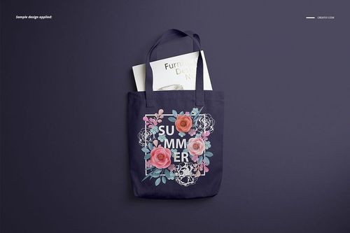 Front view of a polyester tote bag mockup with dark fabric, floral graphic and text, lying on a dark surface.