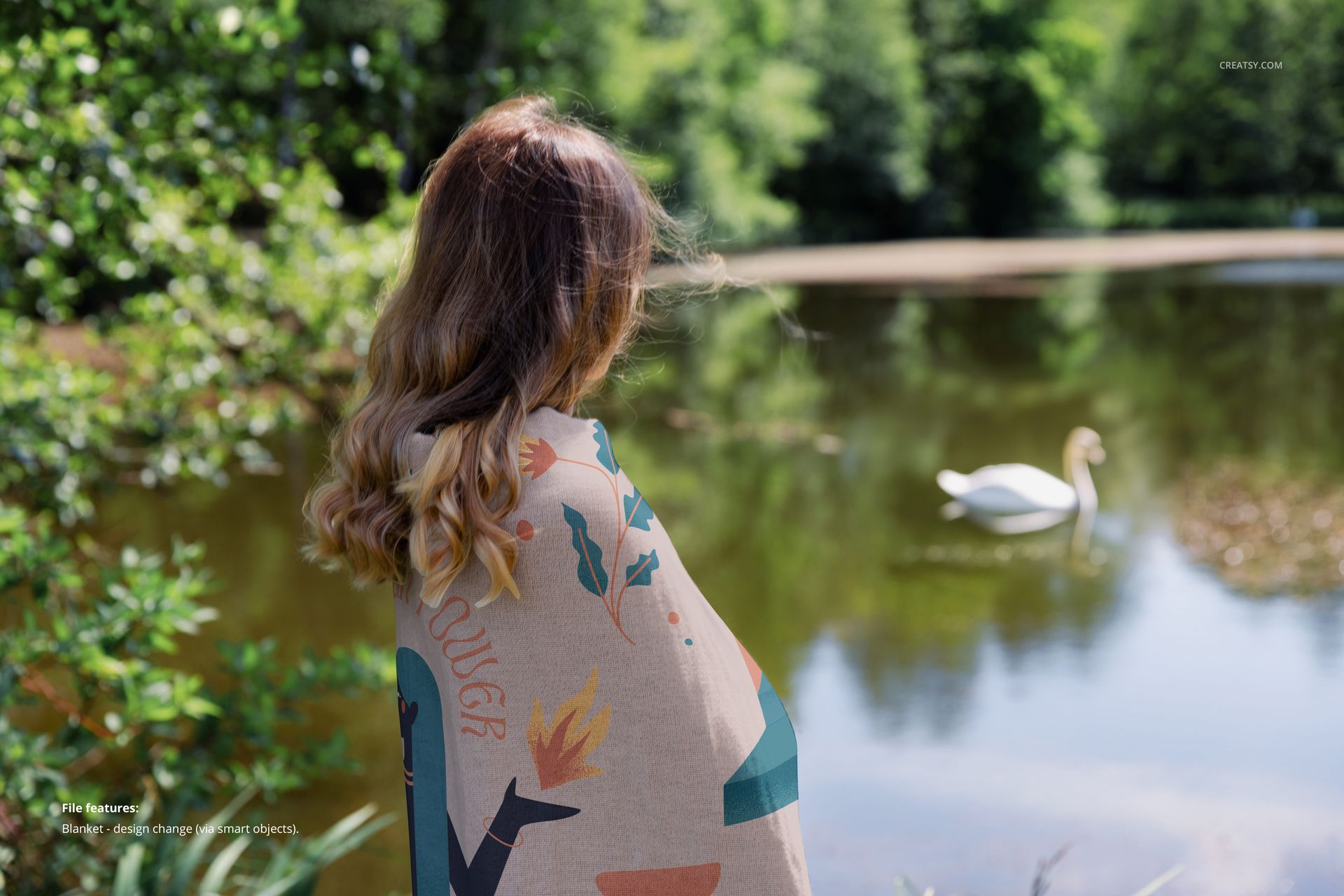 Outdoor scene featuring a PSD mockup of a woven blanket on a woman, facing a tranquil lake with a swan in the distance.