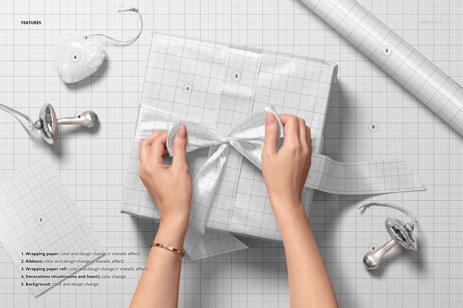 PSD mockup showing hands wrapping a Christmas gift with a ribbon, set on a grid background with holiday props and paper.