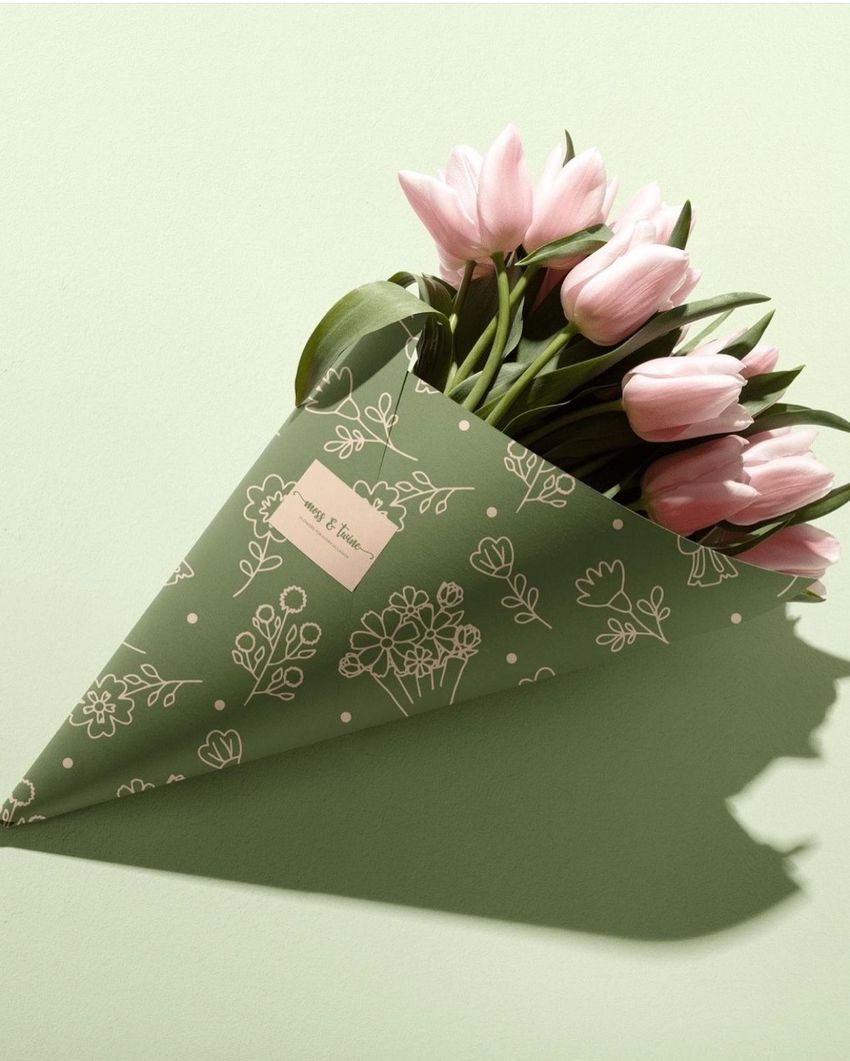 Flower packaging cone mockup featuring pink tulips wrapped in green paper with white floral line art, set on a light green surface.
