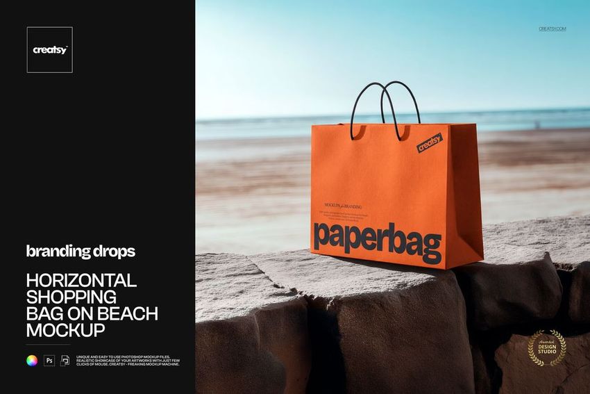 Orange shopping bag mockup with bold black text and handles, positioned on rocks near the ocean, sunlight visible.