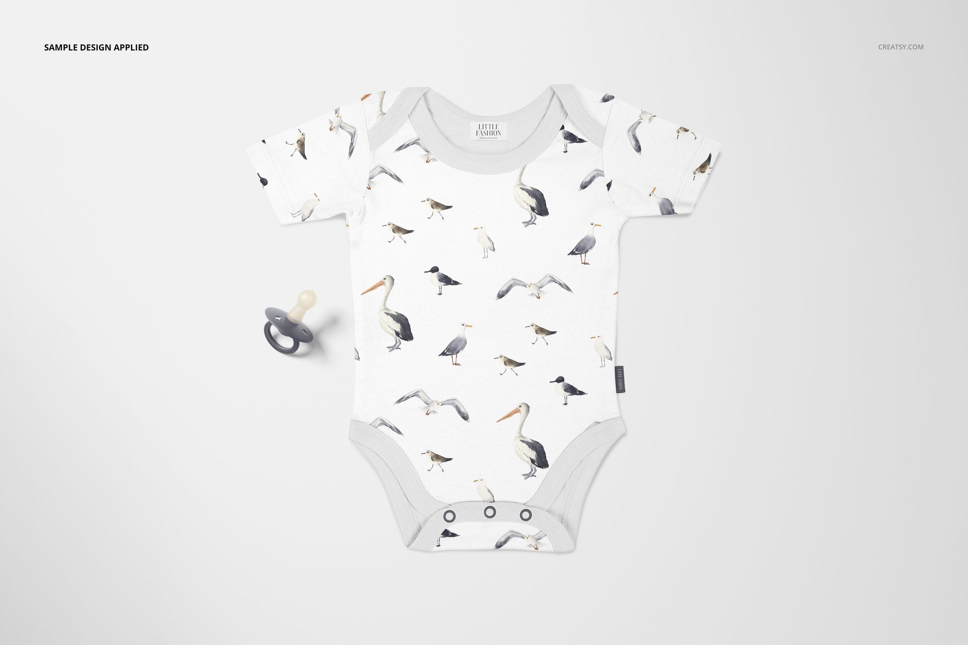 Baby onesie mockup featuring a bird print in gray and beige, laid flat beside a gray pacifier on a light surface.