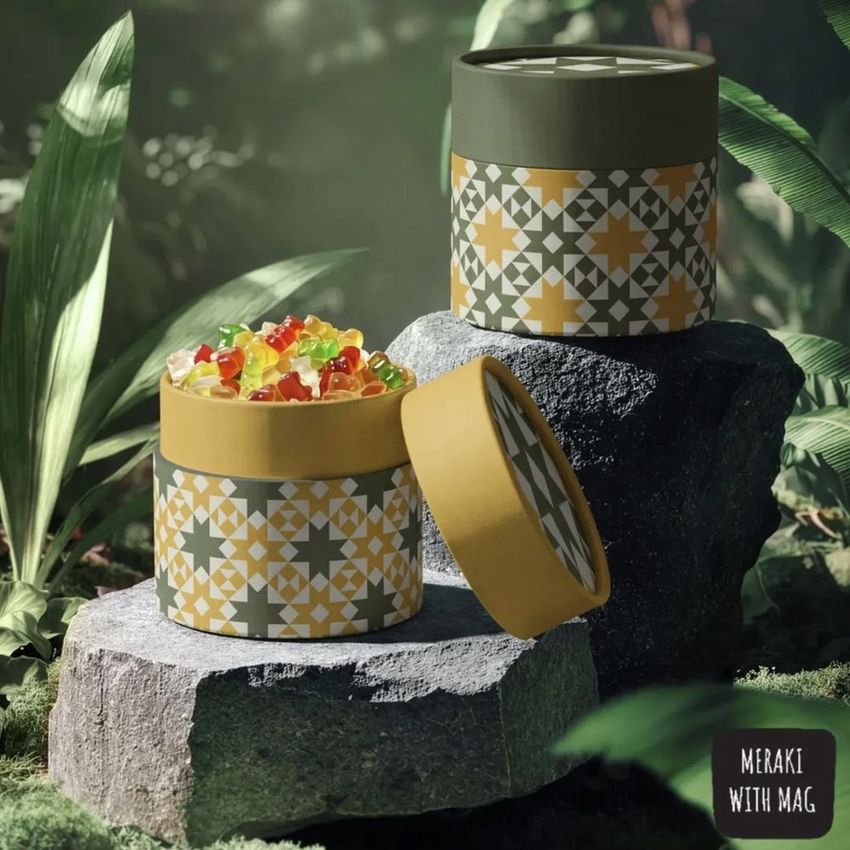 Paper tube packaging mockup with geometric quiltblock patterns, filled with colorful jelly candies, displayed on stone in a lush jungle setting.