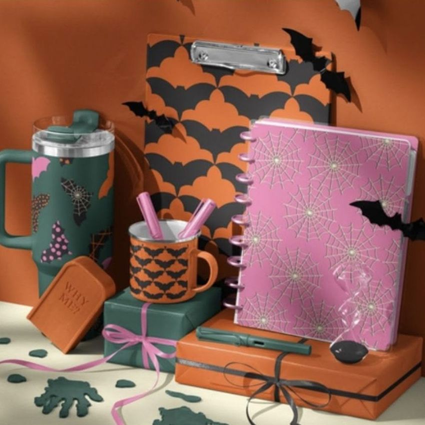 Halloween desk stationery and drinkware mockup featuring orange and black bat patterns, a pink notebook with spiderwebs, and festive props.