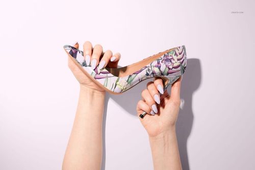 Woman’s hands holding a patterned high heel shoe, side perspective, light pink background, PSD mockup style.